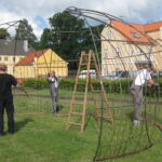 Samling af jernstativerne til pilehytten på plænen.