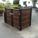 En meget smukt pilehegn opført med lodrette pilesektioner og en dobbelt smedejernslåge til affaldsstativerne.