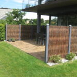 De gråmalede stolper har et flot sammenspil med pilehegnet og huset.