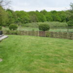 En dejlig have indrammes af et lavt pilehegn som passer perfekt til omgivelserne.